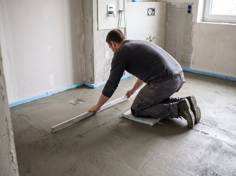 Handwerker zieht Gefälleestrich für eine bodengleiche Dusche ab