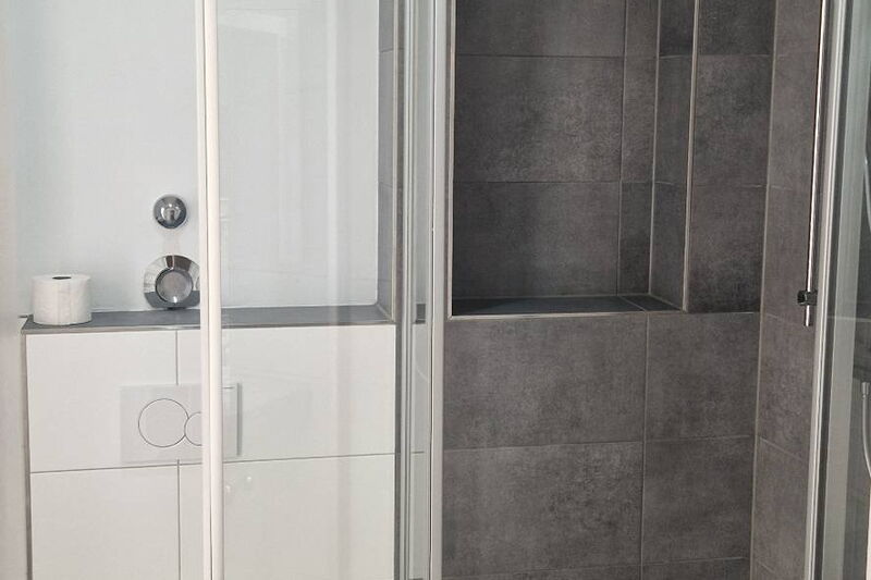 Nachher: Waschtisch, Spiegel und Blick in die neue Dusche mit dunklen Fliesen
