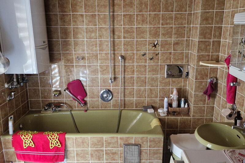Vorher: altes Bad mit braunen Wandfliesen, grüner Badewanne und grünem Waschbecken