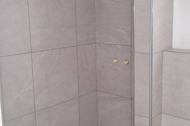 Nachher: bodengleiche Dusche mit Duschrinne, raumhoch gefliest in heller Steinoptik
