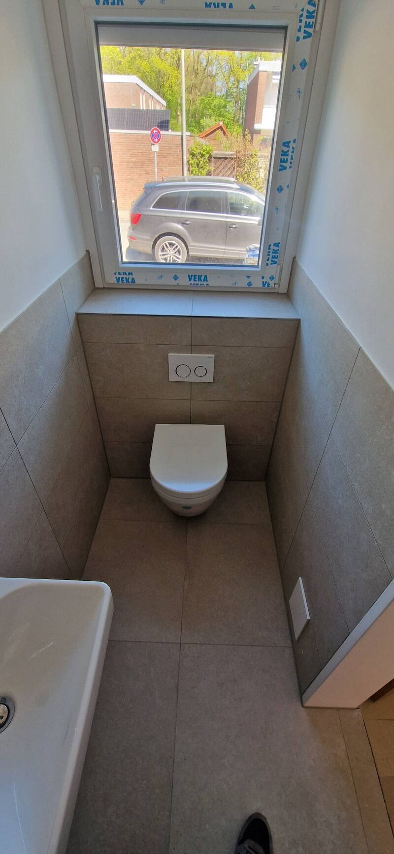 Nachher: Gäste-WC mit Wand-WC, halbhoch gefliesten Wänden in Steinoptik und gefliester Fensterbank