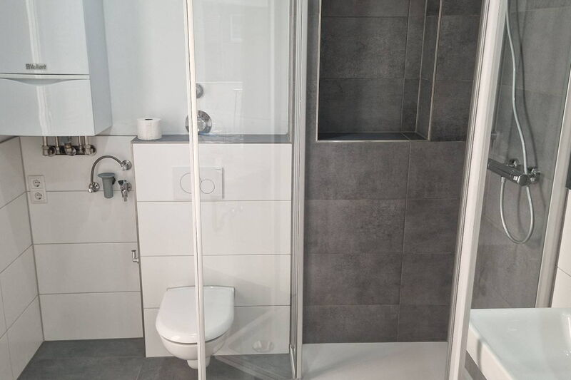 Nachher: Dusche mit Glasabtrennung und anthrazitfarbenen Fliesen, Ablagenische, Wand-WC und weiße Großformatfliesen