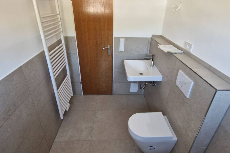 Handtuchheizkörper, Tür, Waschtisch und Wand-WC im neuen Bad mit Fliesen in Sandtönen